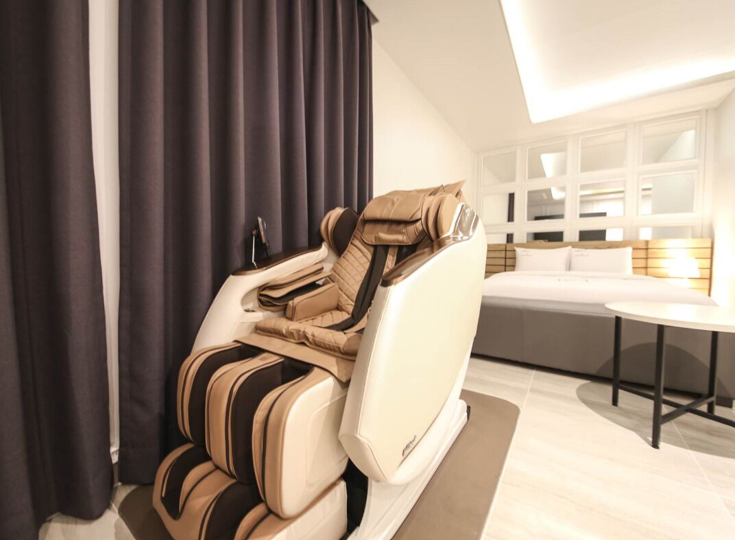 A massage chair in a modern room with a large window, a sofa, and a small table.