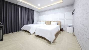 Una habitación de hotel moderna con dos camas, un ventanal con cortinas, un aire acondicionado integrado y un televisor montado en la pared.