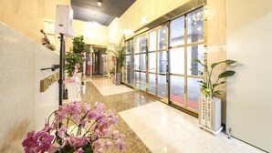 Um hall de hotel com piso de mármore, grandes portas de vidro e plantas em vasos.