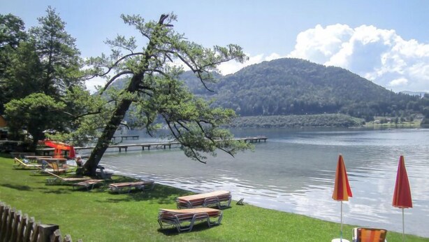 A lakeside view with a wooden deck, picnic tables, and umbrellas.