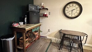Ett kök med en mikrovågsugn, en klocka, en papperskorg och ett träbord.