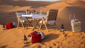 Un coin repas aménagé dans le désert, avec une table, des chaises et des lanternes.
