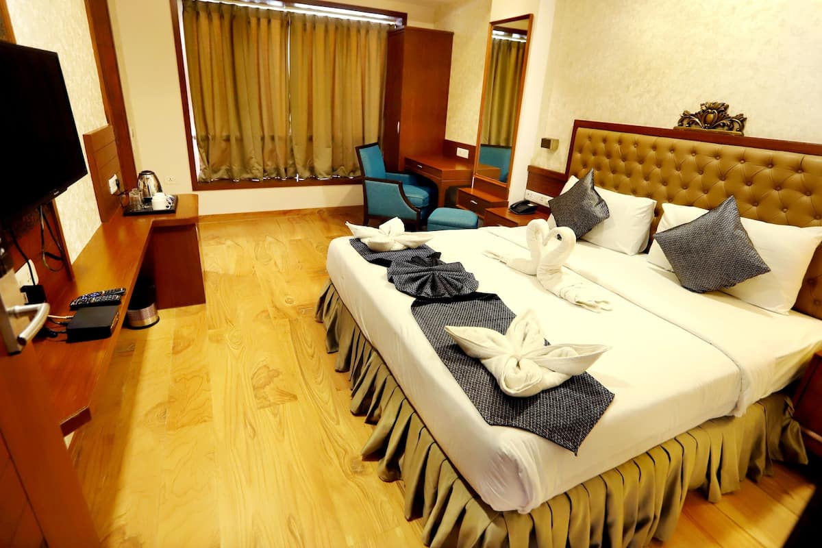 A hotel room with a large bed, a TV, a desk with a chair, and a window with curtains.