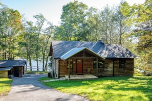 A log cabin with a porch, a chimney, and a small deck. - Cozy Lakefront Retreat w/ Game Room & Hot Tub (McHenry)