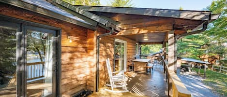 A wooden cabin with a covered porch, large windows, and a deck area.