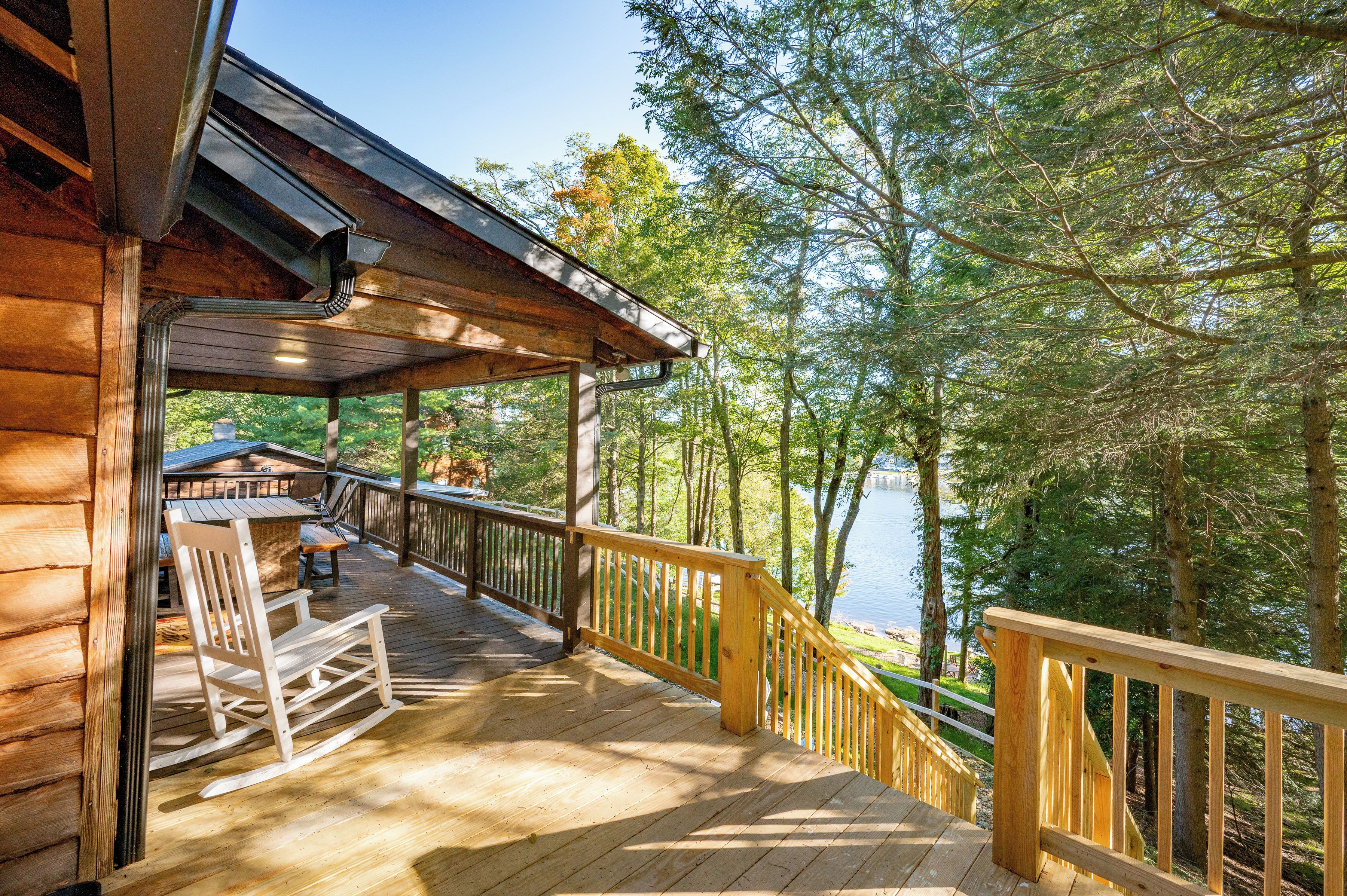A wooden deck with a railing, overlooking a forested area and a body of water.