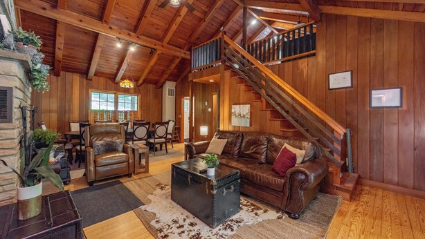 A spacious living room with a leather sofa, a coffee table, and a staircase leading to an upper level. - Cozy Lakefront Retreat w/ Game Room & Hot Tub (McHenry)