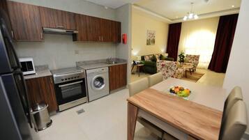 A compact kitchen with a washing machine, a dining area with a table set for two, and a living room with a sofa and a chair.