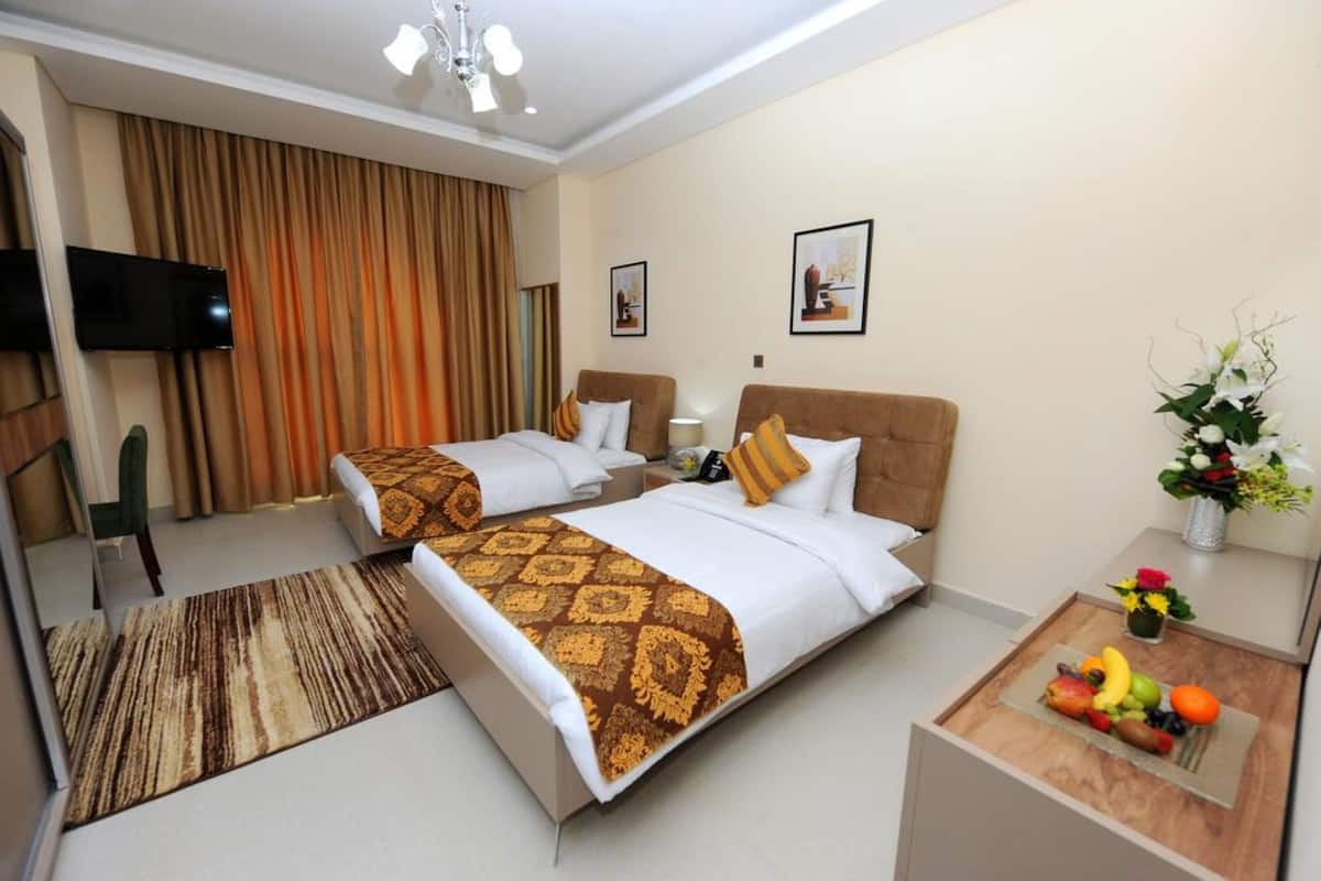 A hotel room with two beds, a TV, a desk with a fruit bowl, and a vase with flowers.