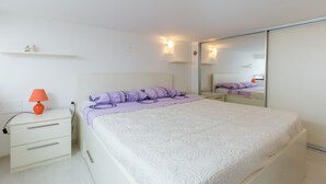 Une chambre à coucher comprenant un lit, une table de chevet, une lampe, un miroir et une commode.