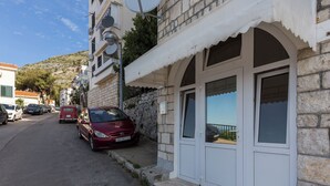 Une rue étroite bordée de voitures garées, un bâtiment en pierre à la façade blanche et un ciel dégagé.