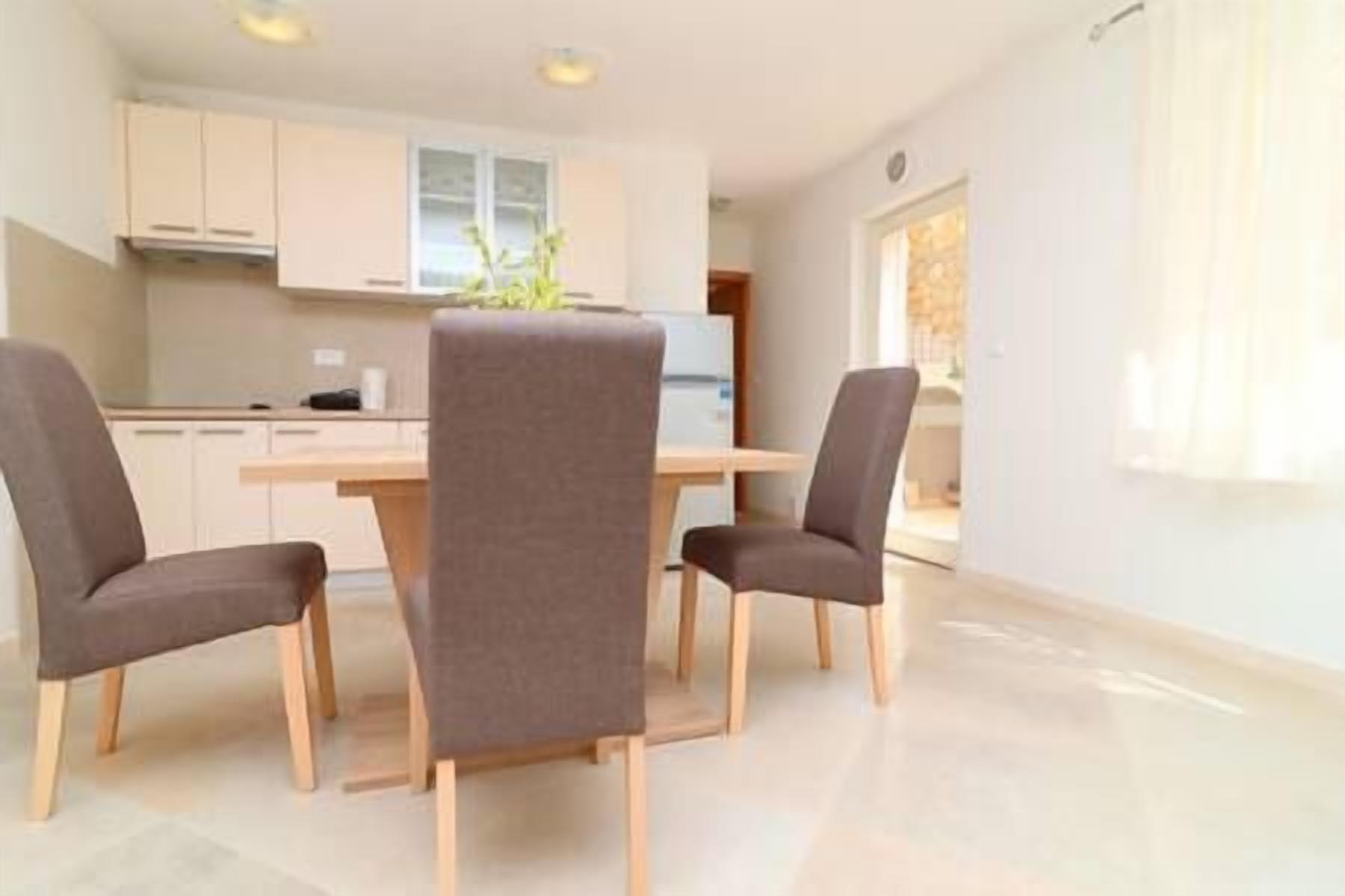 Una cocina moderna con armarios blancos y una isla central. Hay dos sillas con tapicería oscura y una mesa en primer plano.