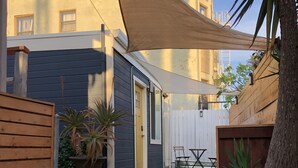 En innergård med ett trädäck, krukväxter, ett vitt staket och en byggnad med en mörk fasad och fönster.
