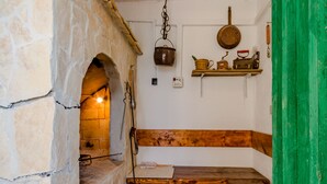 Una cucina con pareti in pietra, un forno a pietra, una panca di legno e mensole piene di utensili da cucina.