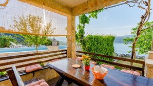 Un terrazzo in legno con tavolo e sedie, affacciato su una piscina e un panorama suggestivo di colline e acqua.