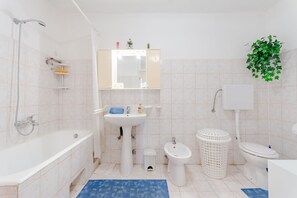 A bathroom with a bathtub, sink, bidet, toilet, and a hanging plant. - Apartment Sea Star (Trogir)