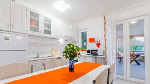 Una cucina moderna con mobili bianchi, un tavolo da pranzo con una tovaglia arancione e vista sull'esterno attraverso una porta in vetro.