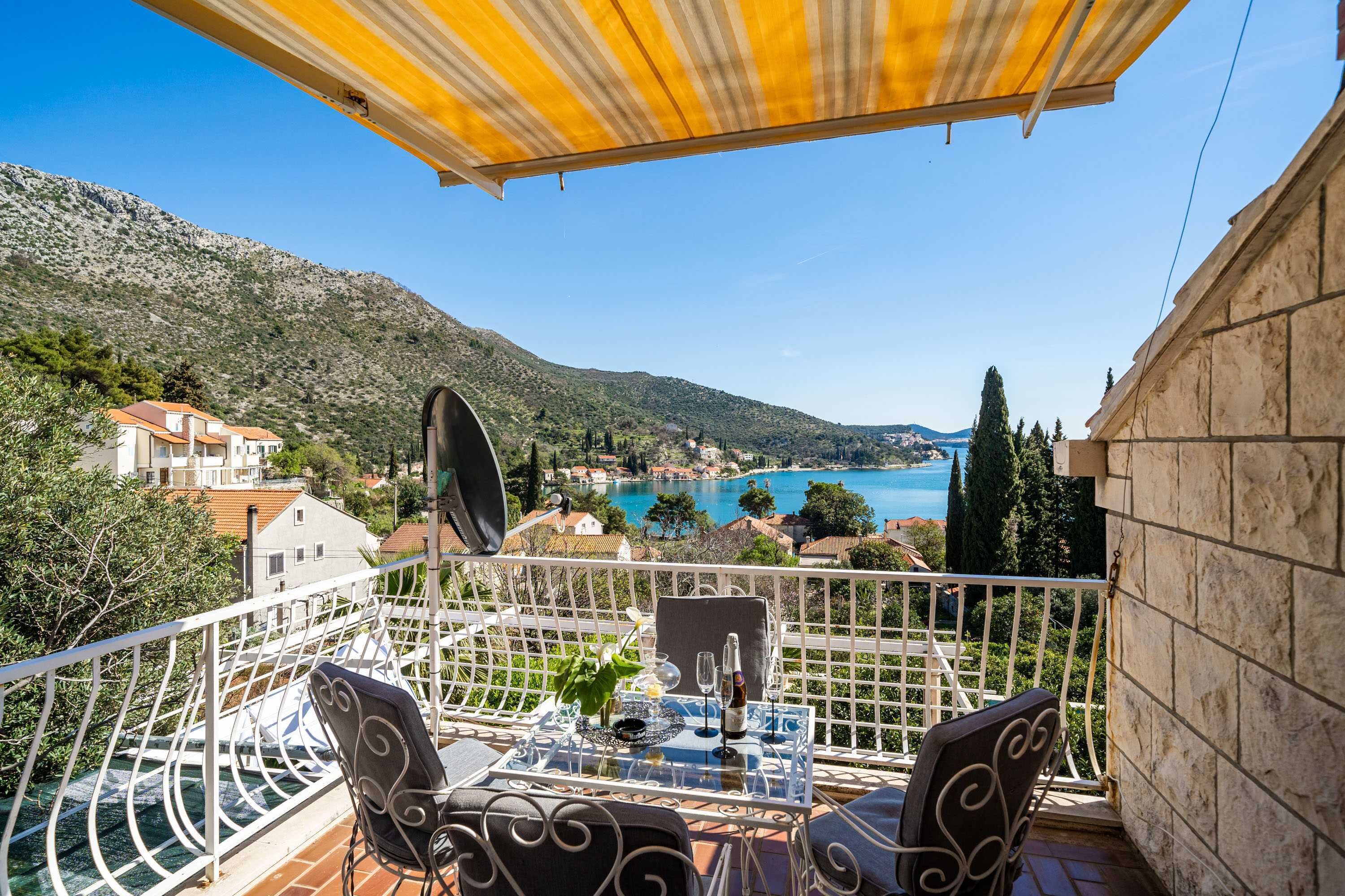 Un balcón con mesa y sillas, con vista panorámica a un lago y montañas.