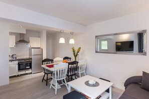 Una cocina compacta con muebles blancos, un comedor con mesa y sillas blancas, y un espejo grande en la pared.