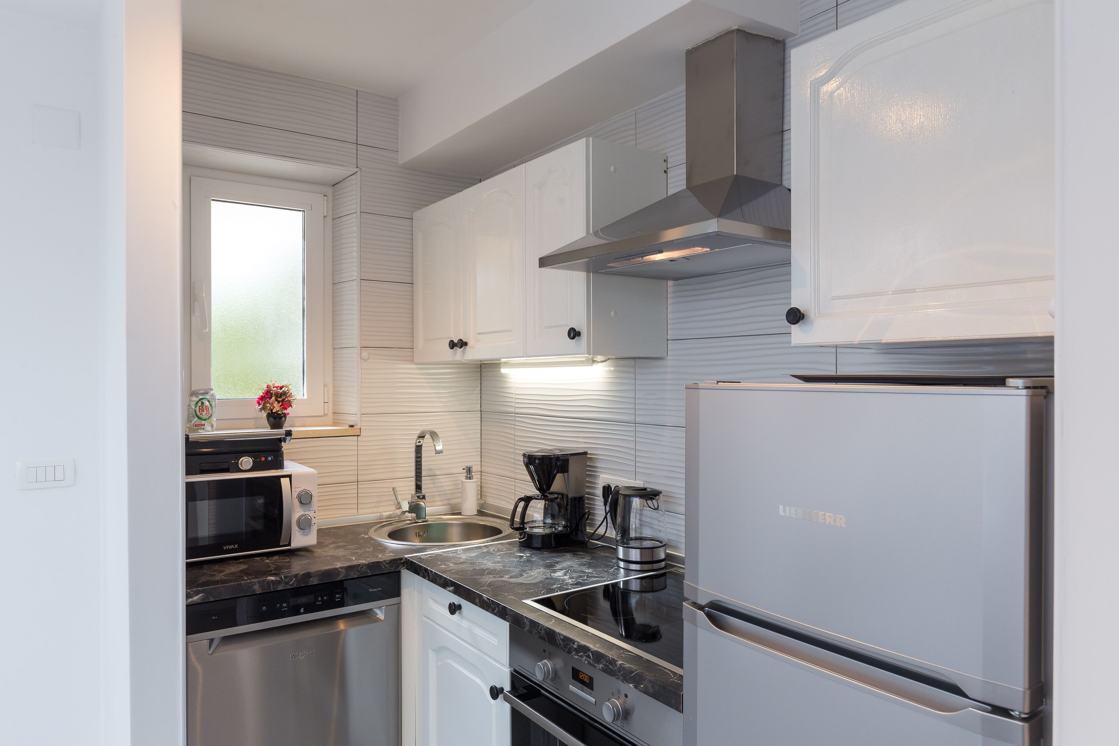 A modern kitchen with white cabinets, a stainless steel refrigerator, a microwave, and a coffee maker.