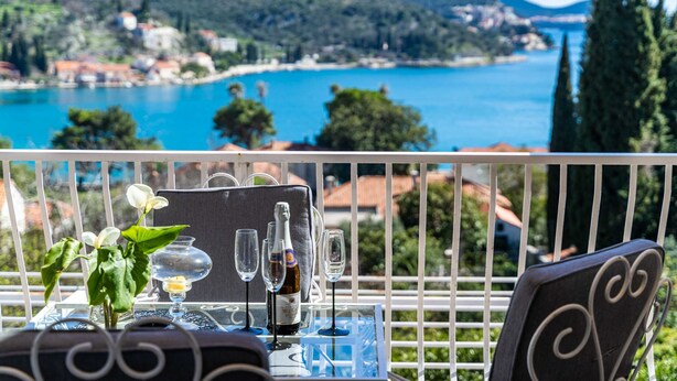 A balcony with a table set for two, overlooking a scenic coastal view. - Apartment Rea Zaton (Dubrovnik)