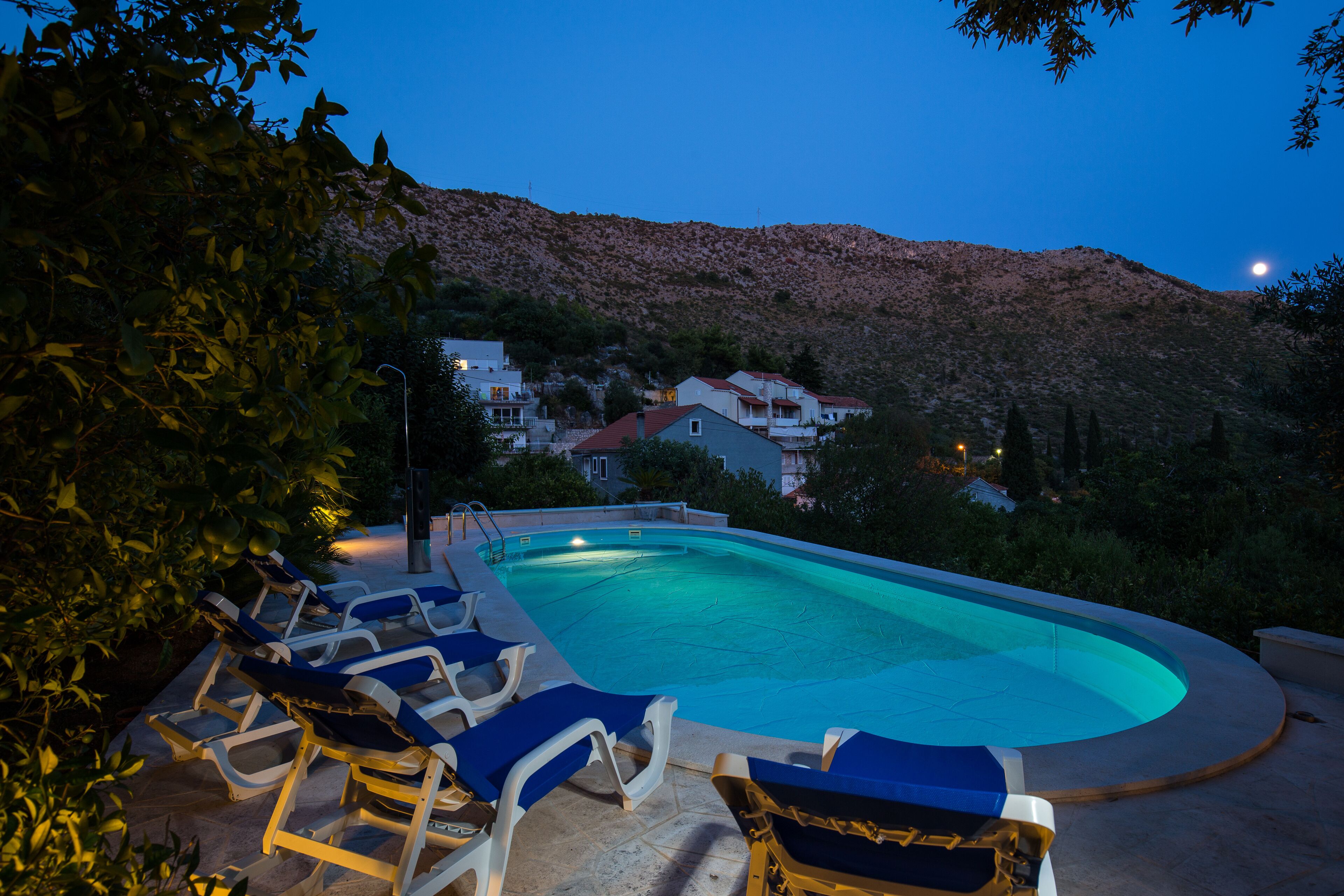Una piscina con sillas de descanso, rodeada por un paisaje montañoso al anochecer.