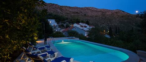 Una piscina con sillas de descanso, rodeada por un paisaje montañoso al anochecer.