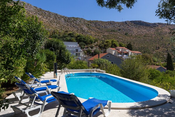 Una piscina con tumbonas, rodeada de vegetación y casas en una zona montañosa.
