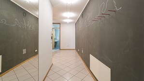 Un pasillo con piso de baldosas, una pared blanca con una lámpara y una pared oscura con un diseño de luz de neón.