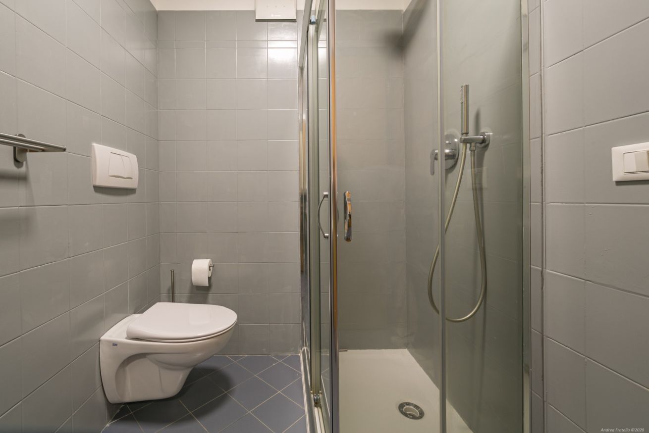 Une salle de bain moderne avec une douche à parois de verre, des toilettes blanches et des murs recouverts de carreaux gris.