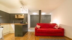 Un espacio habitable compacto con kitchenette, un sofá rojo y una alfombra gris.