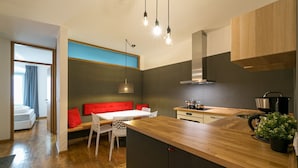 Una cocina moderna con encimeras de madera, estufa integrada y un comedor con sofá rojo y sillas blancas.