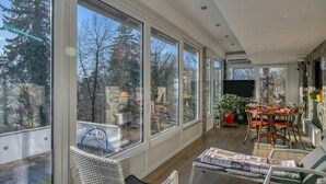A sunlit room with large windows, a dining area with a table and chairs, and a sofa. - Forest Retreat Bonidesa - Terrace & Jacuzzi (Ljubno)