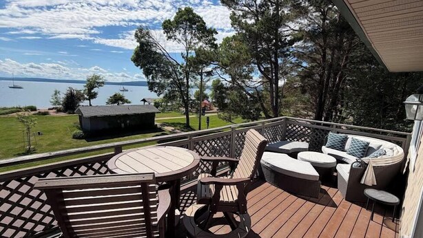 A deck with outdoor furniture, a view of the water, and a small building in the background. - Remodeled Downtown Condo Across the Street from Jo (La Pointe)