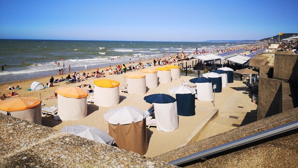 Une plage avec des parasols et des chaises longues, une jetée et l’océan.