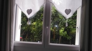 Une fenêtre ornée de deux rideaux blancs, décorés de motifs en forme de cœur et de glands.