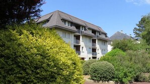Un immeuble résidentiel à plusieurs étages, doté de balcons, entouré d’un espace vert bien entretenu et surplombant un ciel dégagé.