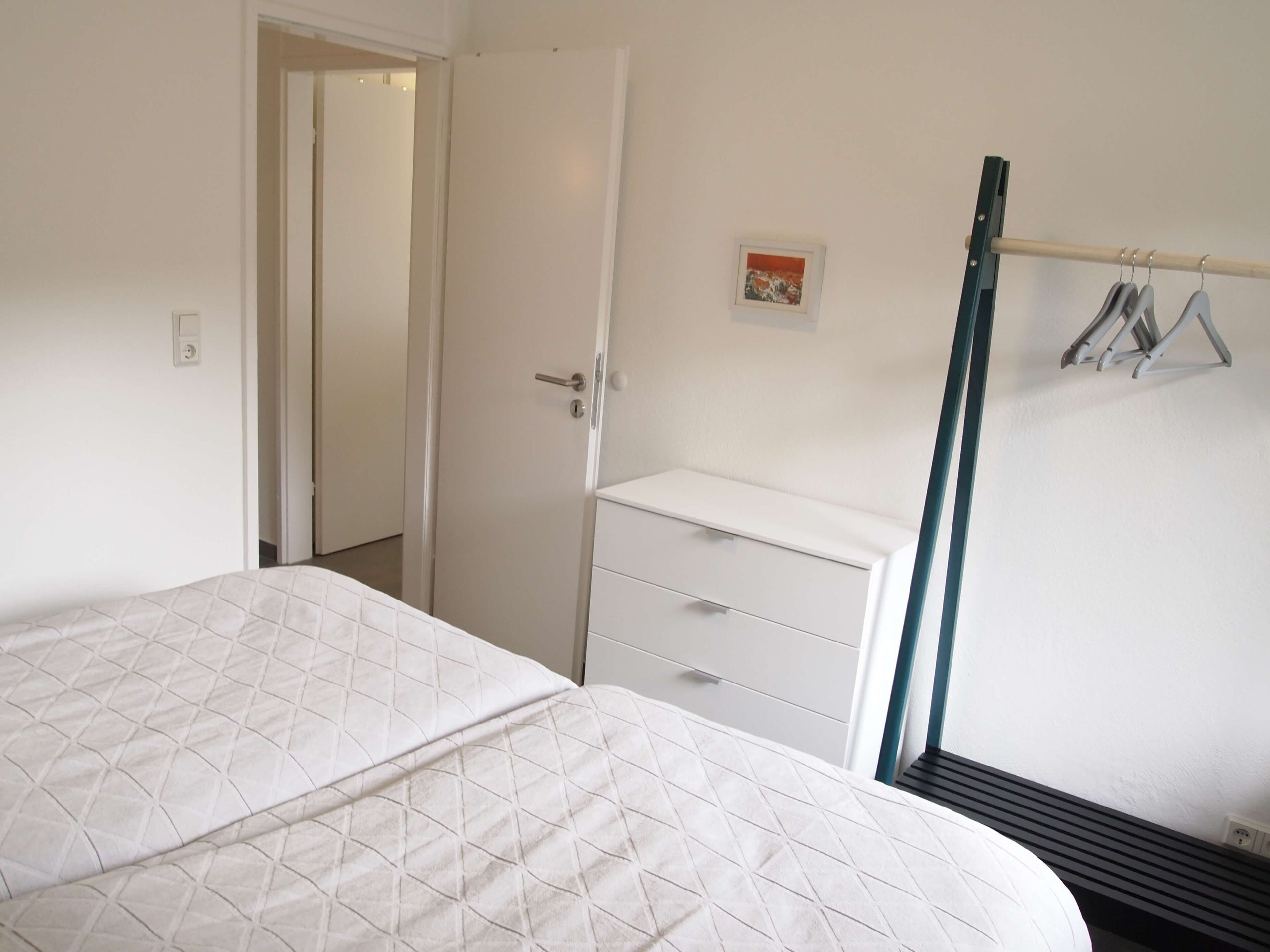A bedroom with a bed, a dresser, a door, and a coat rack.