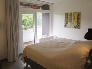 A bedroom with a bed, a window, a door leading to a balcony, and two paintings on the wall.