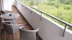 A balcony with wicker furniture and a glass table, overlooking a forested hillside.