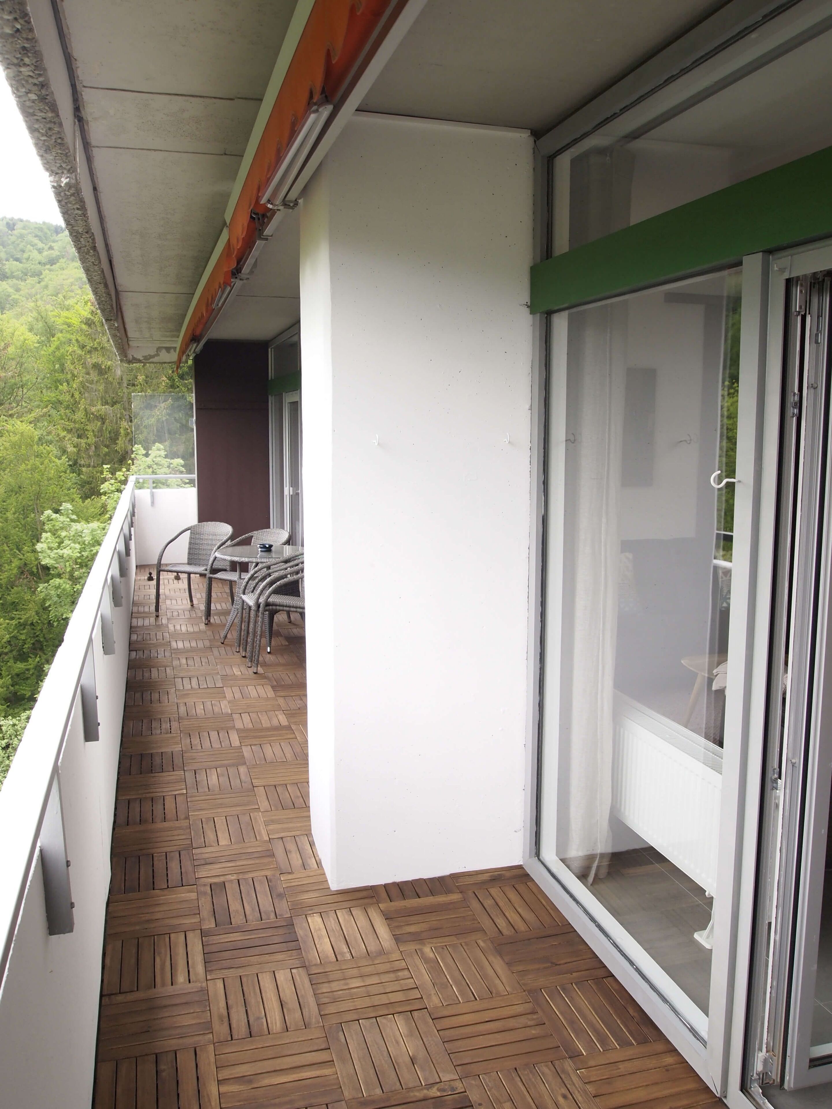 Un balcón con suelo de madera, una mesa con sillas y vistas a la vegetación.