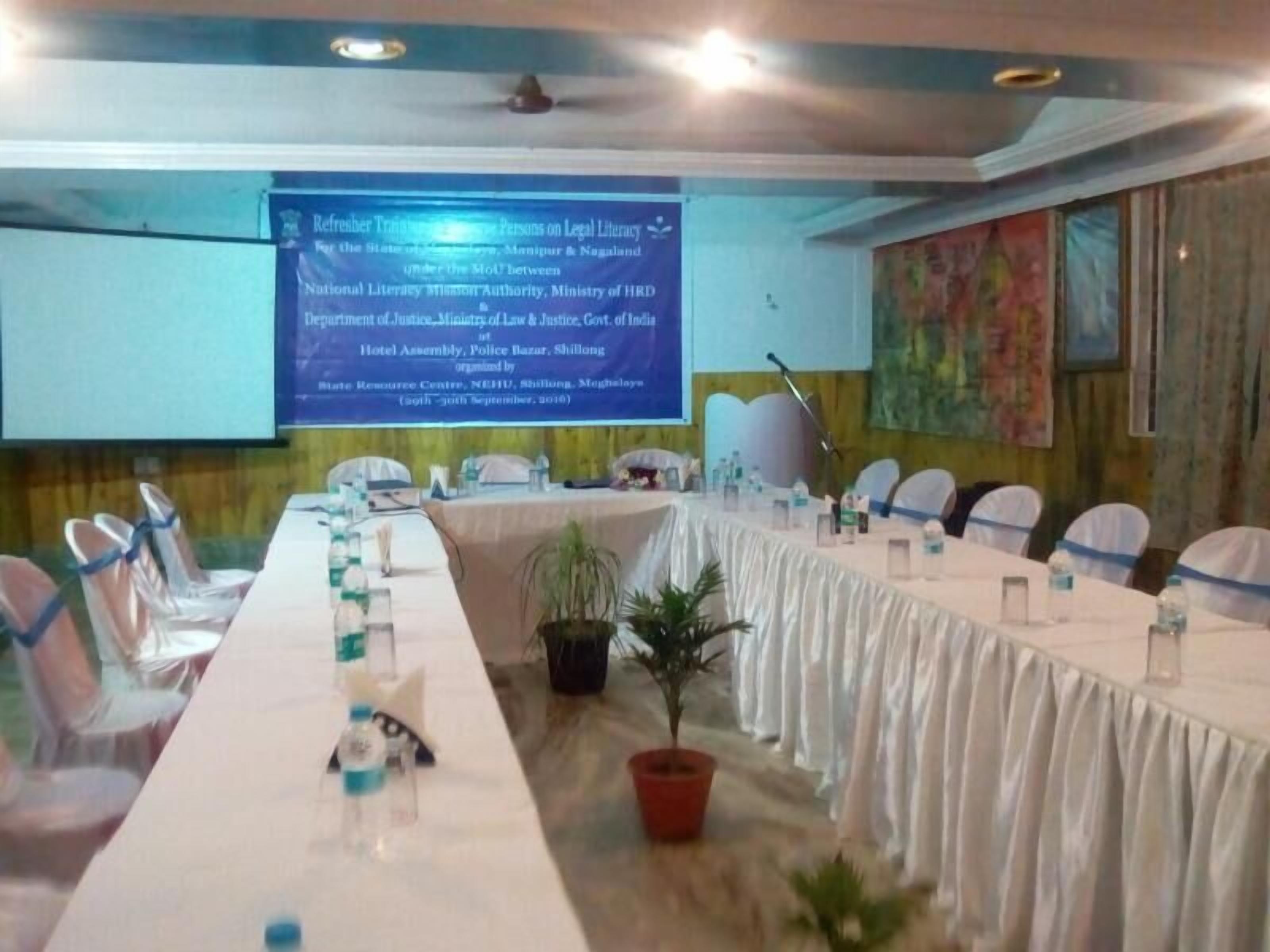A conference room with a long table, chairs, a projector screen, and a microphone.