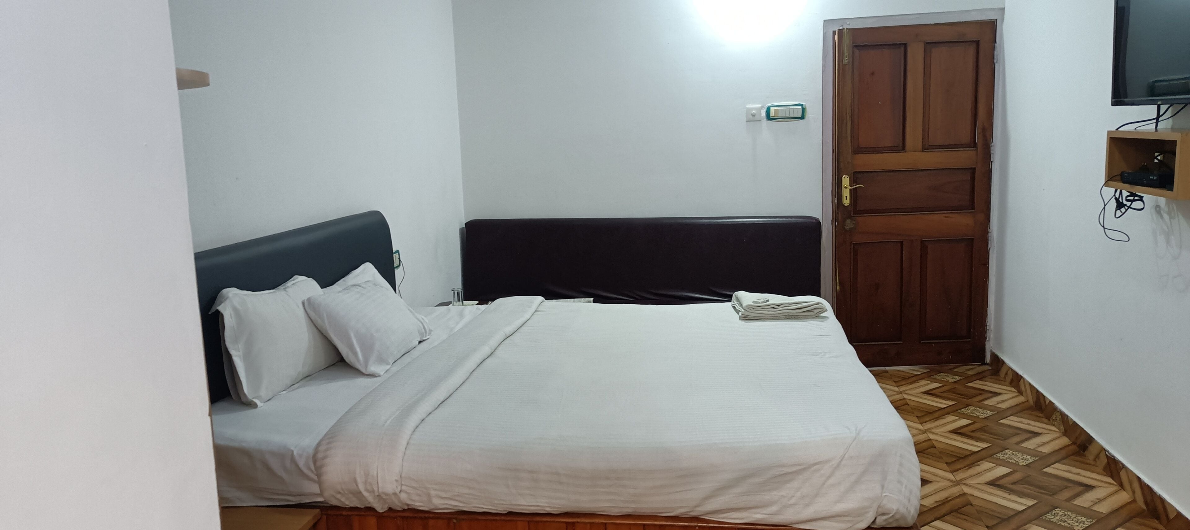 A bedroom with a bed, a wooden door, and a TV mounted on the wall.