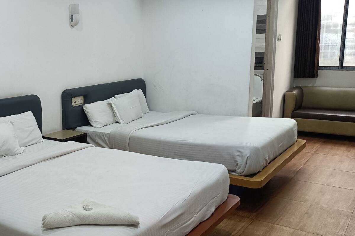 A hotel room with two beds, each with white bedding and headboards. There is a small table between the beds and a window with curtains.