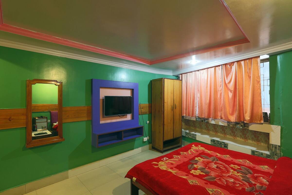 A bedroom with a bed, a television mounted on the wall, a wardrobe, and a bathroom with a sink and mirror.