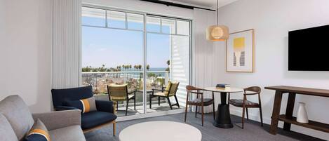 A modern hotel room with a balcony, a sofa, a round table, and a TV.