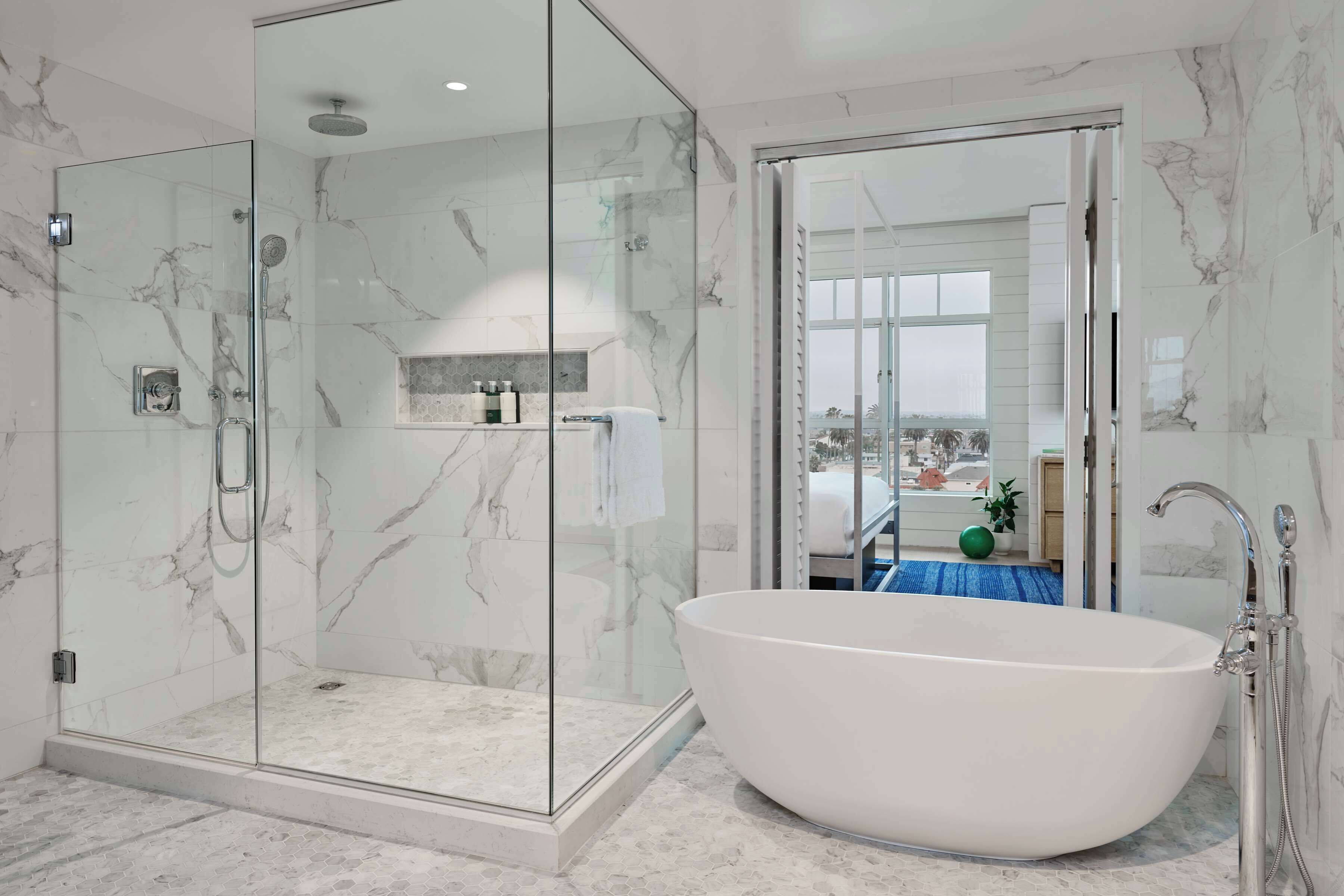 Un baño moderno con ducha de vidrio, una bañera independiente y vistas de la ciudad a través de un ventanal grande.