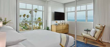 A bedroom with a large bed, a TV, a chair, and a view of the ocean.