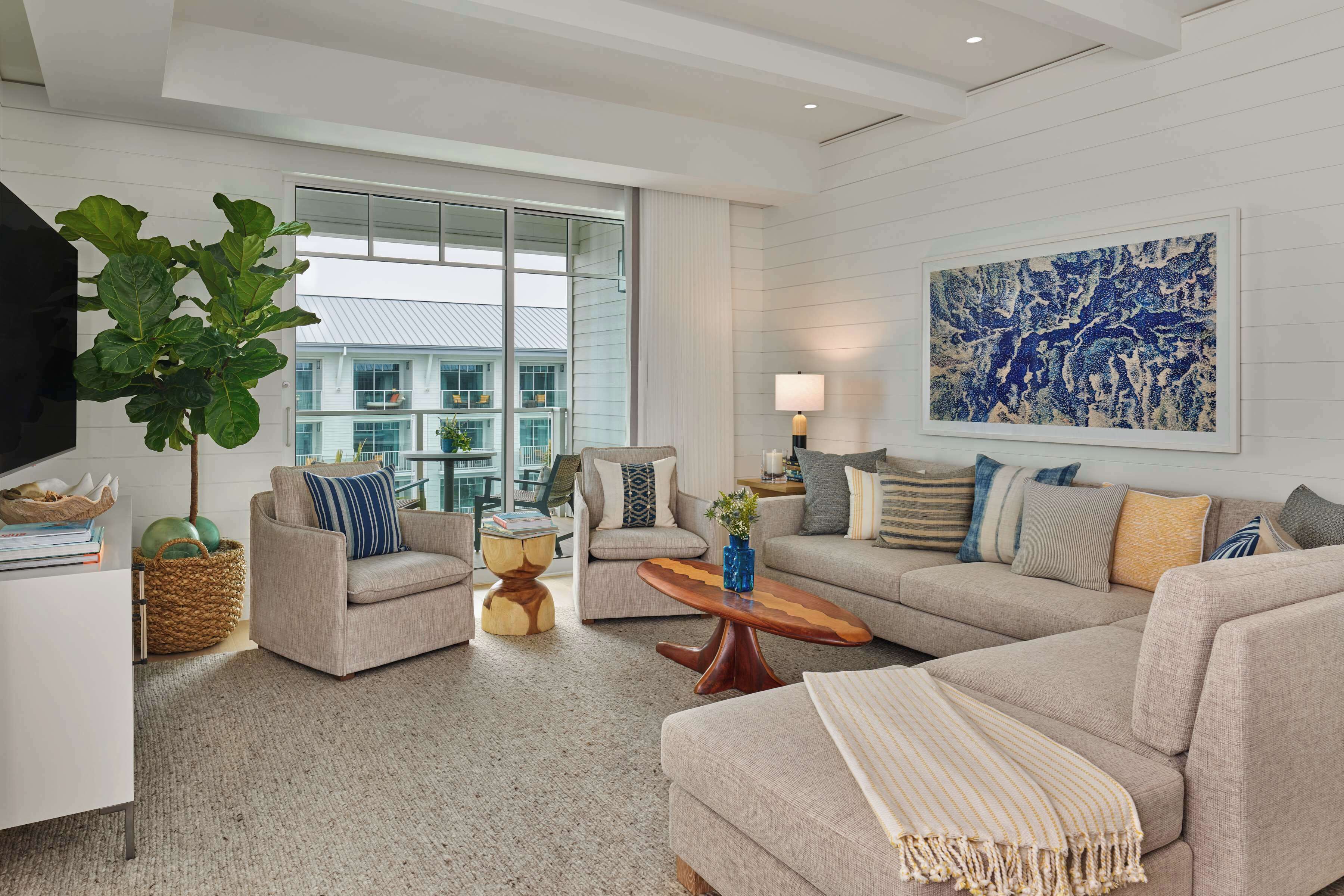 A modern living room with a large window, a flat-screen TV, and a blue abstract painting.