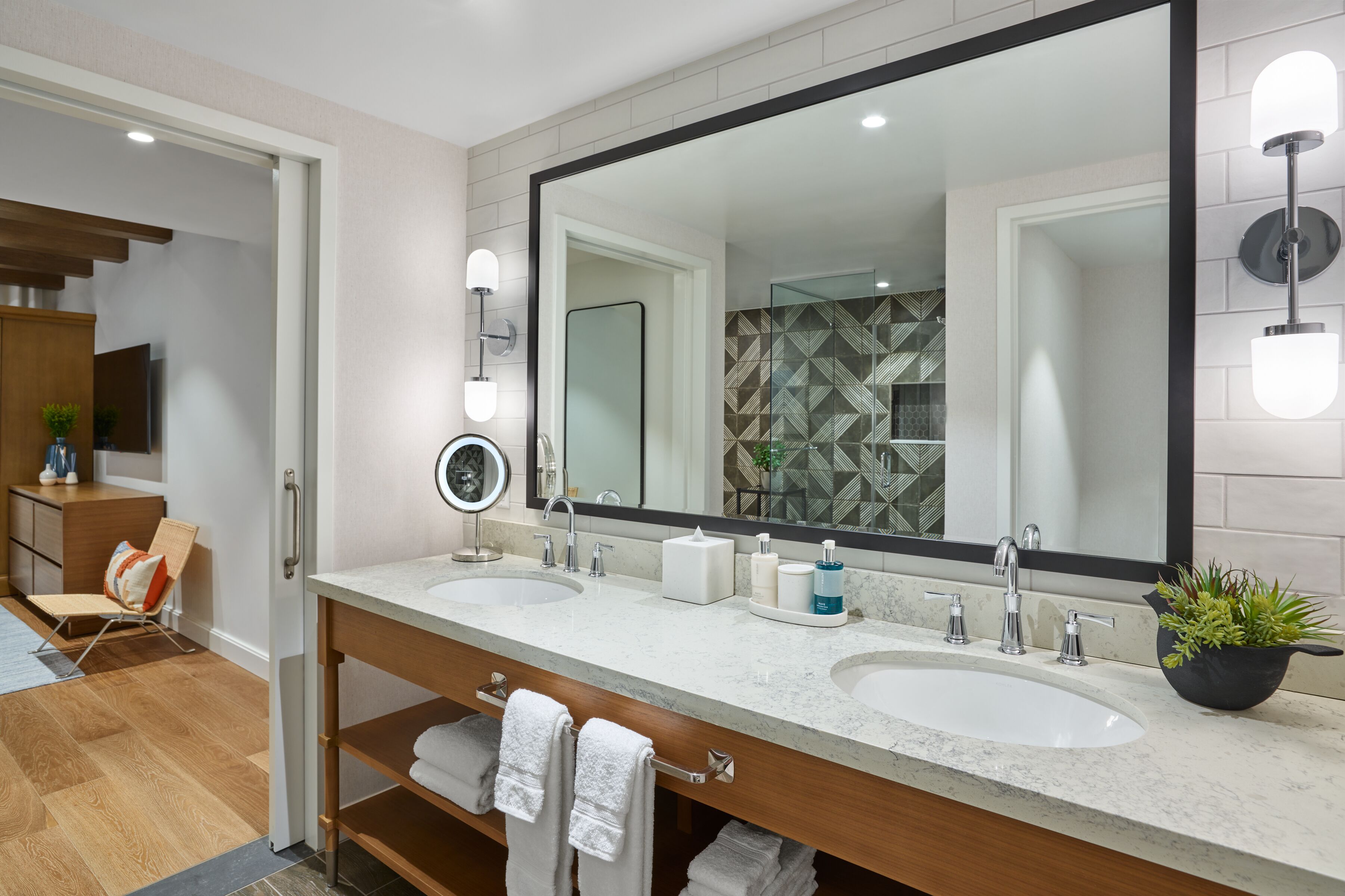 A modern bathroom with two sinks, a large mirror, and a potted plant.